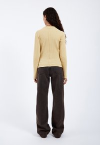 Yellow ribbed long-sleeve top with a center seam, paired with loose-fitting dark brown pants. The fabric appears textured and casual.