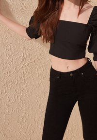 Top corto nero con scollatura quadrata e maniche a sbuffo, abbinato a jeans skinny neri. Tessuto liscio con una silhouette aderente.