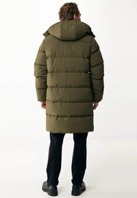 Polstret parka i olivengrøn, med hætte, quiltet design, lang længde og sidelommer, parret med sorte bukser og støvler.