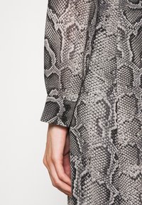 Camicia a maniche lunghe con motivo a serpente in nero e grigio, con dettagli ai polsini bottonati e una texture di tessuto liscia.