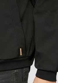Juodas bomber tipo švarkas su raukšlėmis ant rankovų, lygi tekstūra, subtilus spindesys ir oranžinė prekės ženklo etikėtė apatinėje kairėje pusėje.