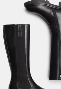 Botas negras hasta la rodilla con exterior de cuero liso, paneles laterales elásticos, cierre de cremallera y suela gruesa para mayor estabilidad.