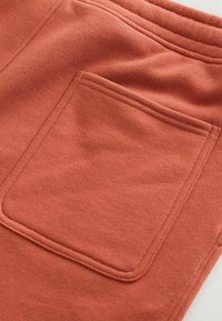 Rustrød sweatshirt stof med en fremtrædende baglomme. Blød tekstur og synlige sømme, der omkranser lommens kanter.