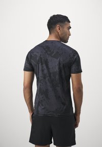 Schwarzes Sportshirt mit einem strukturierten, abstrakten Muster, kurzen Ärmeln und Rundhalsausschnitt, kombiniert mit schwarzen Shorts, von hinten betrachtet.