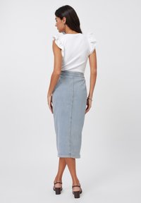 Hvit ribbestrikket topp med volanger på skuldrene, kombinert med et lyseblått jeans-midi skjørt. Modellen har på seg brune sandaler med blokkhel.
