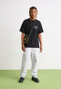 Zwart oversized t-shirt met logo, lichtgrijze baggy jeans, zwarte sneakers en een olijfgroen schoudertasje. Eenvoudig ontwerp en comfortabele pasvorm.