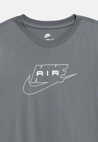 Σκούρο γκρι μπλούζα Nike με λευκό κείμενο "AIR" μέσα σε στυλιζαρισμένο πλαίσιο και μεγάλο λογότυπο Swoosh κάτω από το κείμενο στο στήθος.