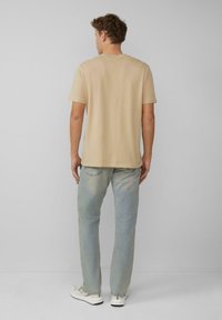 Beżowa bawełniana koszulka z krótkim rękawem, połączona z jasnoniebieskimi dżinsami. Ma klasyczny okrągły dekolt i luźny krój.
