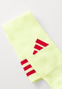 Gule idrettssokker med rød tre-stripes mønster og logo. Teksturert stoff, ankellengde, med kontrasterende røde aksenter.