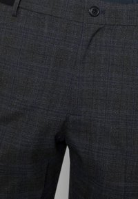 Grå rutiga byxor med en texturerad tyg med blå och svarta linjer. Inkluderar en enkel svart knapp vid midjan.