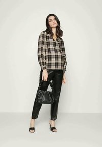 Blusa xadrez em preto e bege, com volantes e mangas bufantes, combinada com calças pretas em couro sintético e uma bolsa preta.