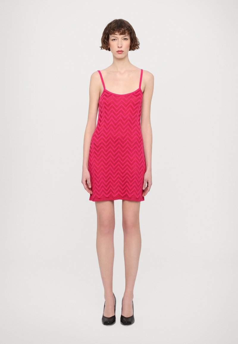 Abito rosa a zig zag con spalline sottili, di lunghezza fino al ginocchio. Realizzato in tessuto morbido, presenta una linea dritta e una vestibilità comoda. Scarpe nere con tacco alto.