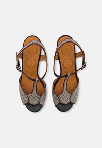 Footwear with a patterned fabric upper featuring geometric designs in black and white, brown leather accents, and an adjustable ankle strap.