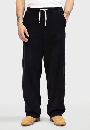 Pantalones de pana negra con un corte relajado, presentando una cintura ajustable con cordón y bolsillos laterales. Textura suave y diseño de pierna ancha.