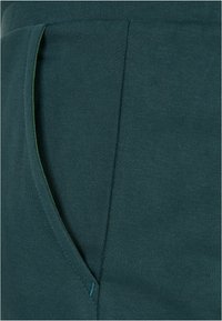 Pantaloni jogger din bumbac în amestec teal, cu un buzunar lateral, având cusături contrastante verzi și o finisare moale, texturată.