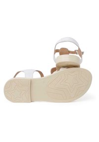 Sandale blanche avec des accents bronzés, design ouvert, semelle plate en caoutchouc avec un motif étoilé et bride de cheville réglable pour un ajustement sécurisé.