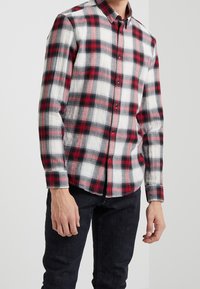 Rood, zwart en witte geruite blouse in lichtgewicht stof met lange mouwen en een afgeronde zoom. Voorzien van een klassieke kraag en knoopsluiting.