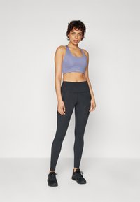 Lys lilla sportsbh og høyt midjesvart leggings laget av elastisk stoff, med en glatt tekstur og uten synlige mønstre eller hardware-detaljer.