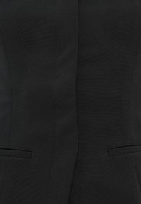 Schwarzer maßgeschneiderter Blazer, strukturiertes Design, glattes Material, zwei Fronttaschen und dezentes Texturmuster. Klassischer Revers und taillierte Silhouette.
