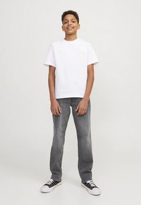 Λευκό κοντομάνικο t-shirt, ανοιχτό γκρι τζιν με ίσια μπατζάκια, μαύρα και λευκά αθλητικά παπούτσια. Το ντύσιμο έχει απλό, καθημερινό σχέδιο.