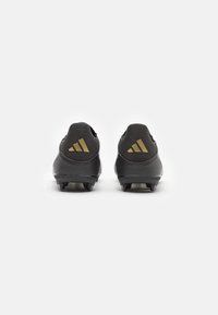 Botas de fútbol negras con una superficie texturizada, presentan detalles en dorado y un distintivo logo triangular en el talón. Suela con tacos para tracción.