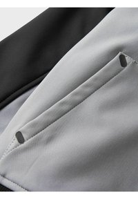 Graue und schwarze Stoffdetails mit einer glatten Textur, schrägen Nähten und einer kleinen Tasche mit abgerundeter Aussparung für besseren Zugriff.