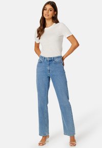 T-shirt bianco leggero con maniche corte abbinato a jeans di denim blu a vita alta. I jeans presentano una gamba dritta e un classico design a cinque tasche.