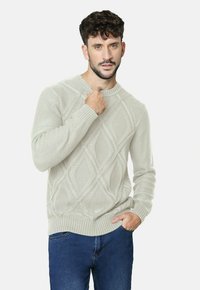 Suéter de punto gris claro con un patrón de diamantes, con puños y dobladillo acanalados, combinado con jeans azules. El diseño es texturizado y acogedor.