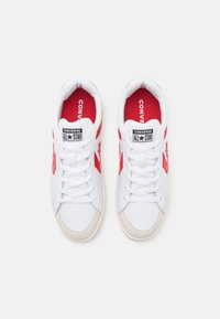 Adidași albi cu accente roșii și logo, având un superior din piele netedă, căptușeală din material textil, închidere cu șireturi și o talpă din cauciuc bej.