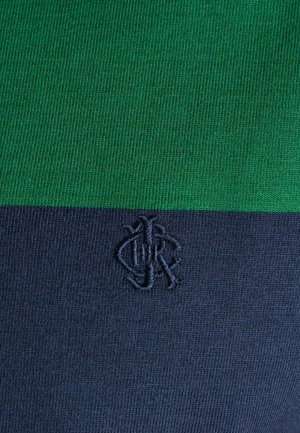Grüner und dunkelblauer Rippenstoff mit einem kleinen, dunklen bestickten Monogramm-Logo, das mittig auf dem dunkelblauen Abschnitt platziert ist.