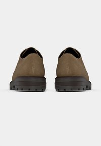 Καφέ σουέντ παπούτσια με στρογγυλεμένη πίσω πλευρά, με υφή και σκούρα λαστιχένια σόλα με αντιολισθητικά. Ο σχεδιασμός είναι μίνιμαλ χωρίς ορατές λεπτομέρειες.