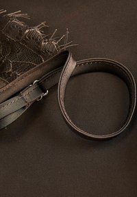 Σκούρο καφέ ύφασμα με λεπτή υφή, με δαντελωτή άκρη και ρυθμιζόμενο λουράκι με μεταλλικούς κρίκους.