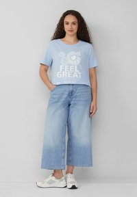 Lichtblauwe katoen t-shirt met witte grafische tekst; gecombineerd met wijdvallende lichtblauwe jeans. De jeans hebben een rafelige zoom en zakken.