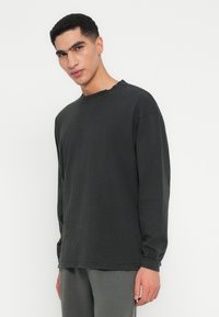 T-shirt a maniche lunghe nera in cotone, con una vestibilità comoda, dettagli di cucitura sottili e un orlo leggermente sfilacciato.