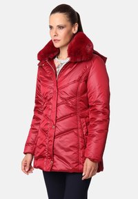 Chaqueta acolchada roja con un cuello forrado de piel. Presenta costuras diagonales y botones de presión. El material tiene un acabado brillante y una textura suave.