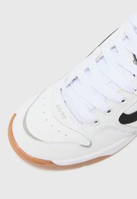 Hvide sneakers med sorte detaljer. Har en glat læderoverdel, perforerede detaljer, flade hvide snørebånd og en tekstureret gummisål.