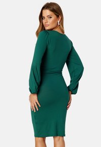 Zelené šaty s dlouhým rukávem, dobře padnoucím korzetem, balónovými rukávy a délkou ke kolenům. Hladká, elastická tkanina s mírným leskem.