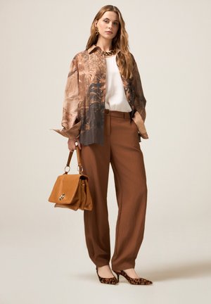Pantalons larges marron associés à une chemise à motifs marron et crème, un haut blanc, des escarpins à imprimé animal, et un sac à main beige avec des accents métalliques.