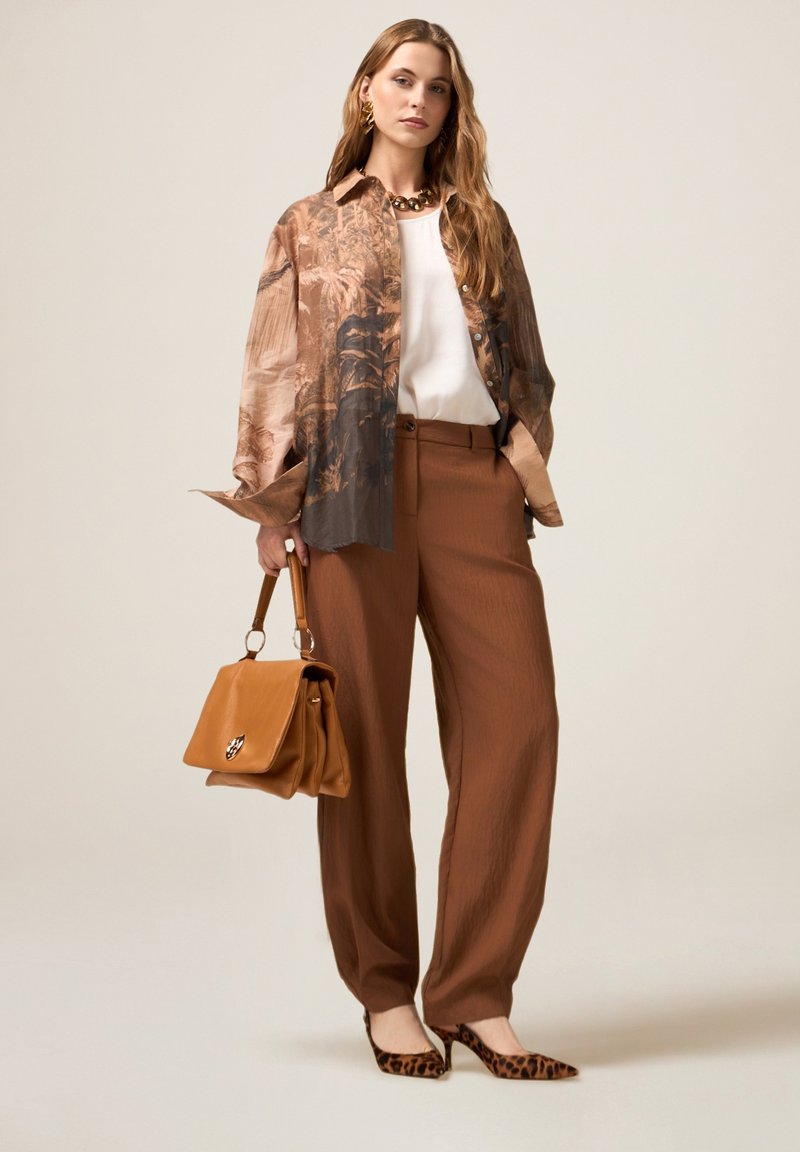 Pantalones de pierna ancha marrones combinados con una camisa estampada en marrón y crema, una blusa blanca, tacones con estampado animal y un bolso color beige con accesorios metálicos.