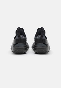 Chaussures de sport noires avec une semelle en caoutchouc texturé, une tige flexible, des languettes de traction et un talon renforcé pour un soutien et un confort accrus.