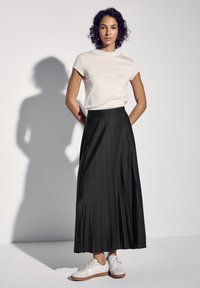 Zwarte geplooide rok met een gestructureerde afwerking, gecombineerd met een aansluitend lichtgekleurde t-shirt en witte sneakers met tan accenten.