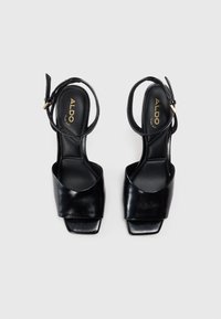 Sandalias de tacón alto negras con un acabado de cuero suave, open toe y una delicada correa en el tobillo. Presentan un elegante diseño de punta cuadrada.