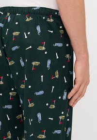 Pantalonii de pijama verzi au un model jucăuș cu temă de golf, prezentând steaguri, mingi de golf și crose. Talie elastică pentru confort și adaptare.