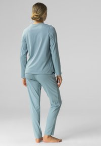 Jasnoniebieska bluzka z długim rękawem i pasujące spodnie uszyte z miękkiego materiału, charakteryzujące się luźnym krojem i rozcięciami po bokach bluzki dla większego komfortu.