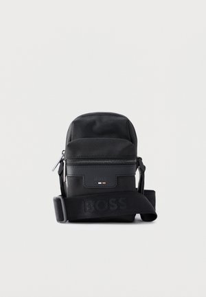Čierna kompaktná kabelka cez rameno s predným vreckom na zips, nastaviteľným popruhom s vyrazeným nápisom "BOSS" a textúrovaným dizajnom látky.