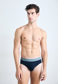 Herenboxers in donkerblauwe stof met een gladde textuur, voorzien van een lichtgrijze elastische tailleband met het "SCHIESSER" logo erop gedrukt.