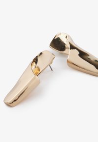 Orecchini metallici oro con una finitura liscia e lucida, caratterizzati da un design curvo e una chiusura a perno. Forma moderna e scultorea.