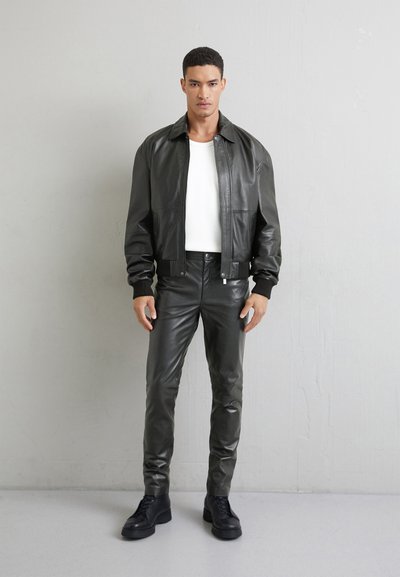 Mörkgrön läderjacka med ribbade mudd, kombinerad med matchande slimfit läderbyxor. Modellen står framför en ljusgrå bakgrund.