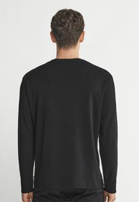 Svart långärmad tröja, rundad halsringning, slät textur, standardpassform, med rak nederkant och subtila sömnadsdetaljer vid krage och manschetter.