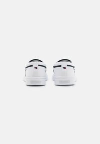 Ein Paar weiße Low-Top-Sneaker mit schwarzem Rand, kleinen roten, weißen und blauen rechteckigen Logos an den Fersen und "HILFIGER"-Branding auf den Sohlen.